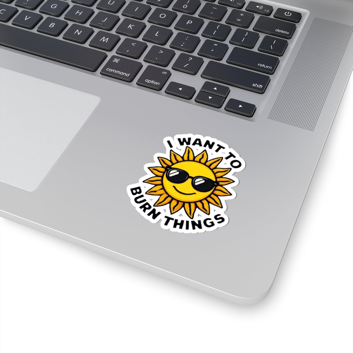 Laptop with a sun-shaped sticker that says 'I want to burn things' on a white background