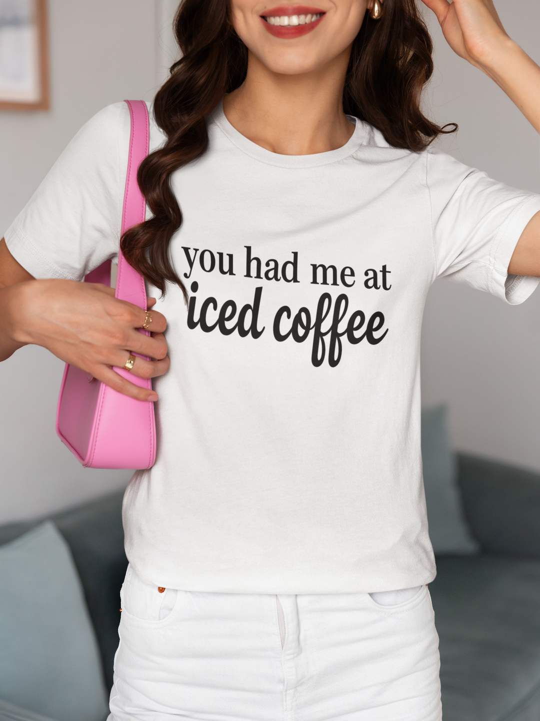Person wearing a white t-shirt with 'you had me at iced coffee' text, holding a pink bag.