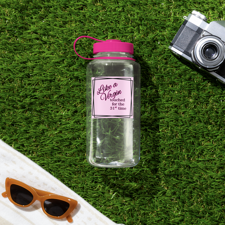 Clear water bottle with pink cap and Like a Virgin sticker on grass with sunglasses and camera