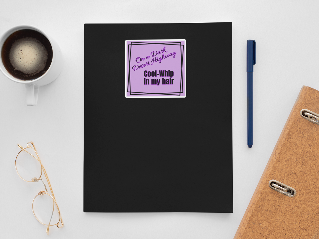 Black notebook with a purple sticker on a white surface with a cup, pen, and glasses.