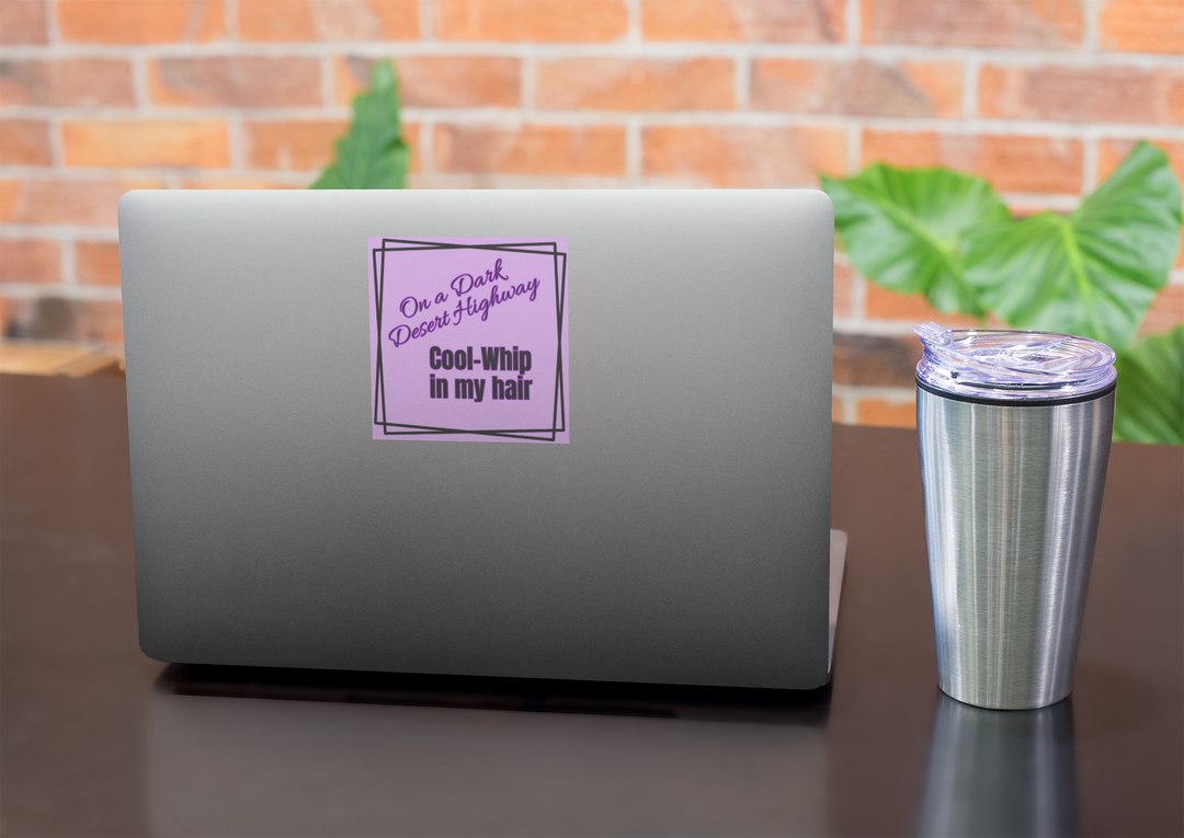 Laptop with a purple sticker on a desk with a tumbler, against a brick wall background