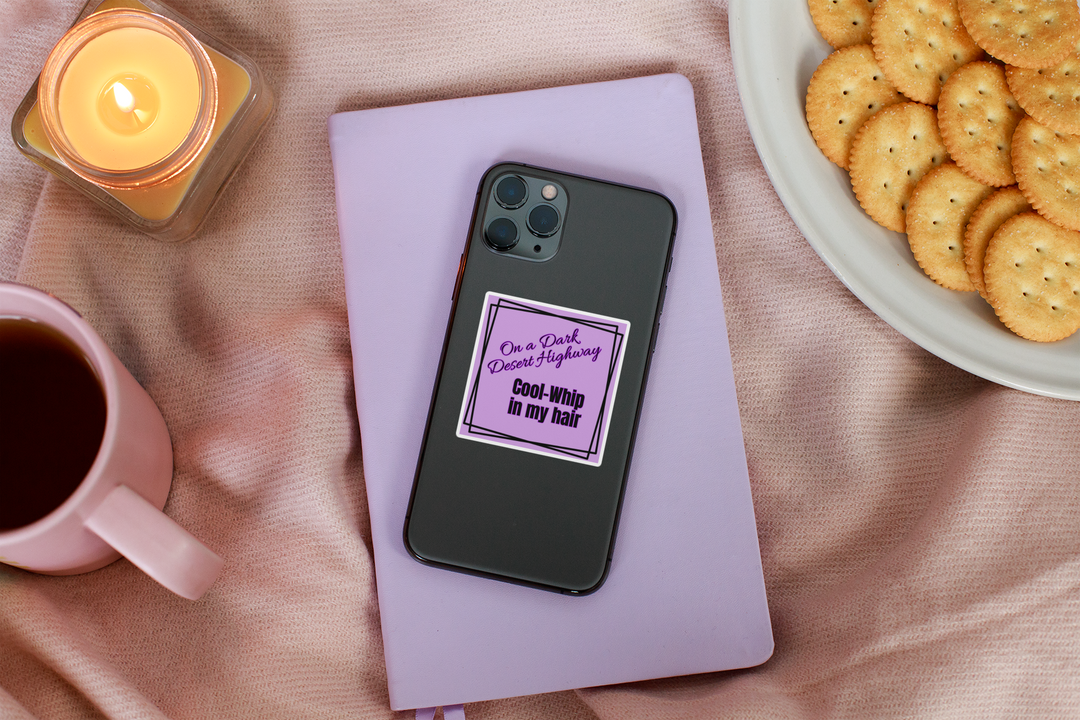 Phone with a purple case on a pink surface with a candle, mug, and plate of cookies.