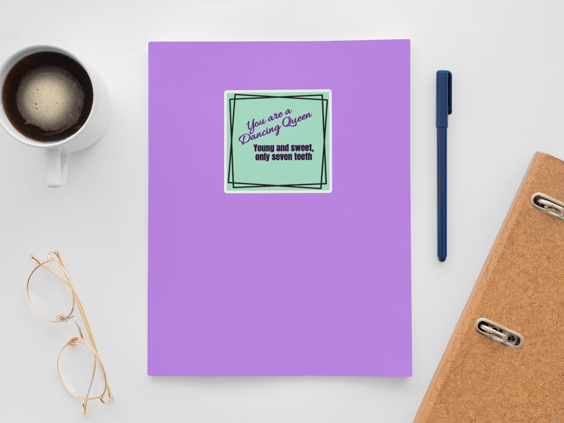 Purple notebook with a sticker, coffee cup, glasses, pen, and phone on a white surface