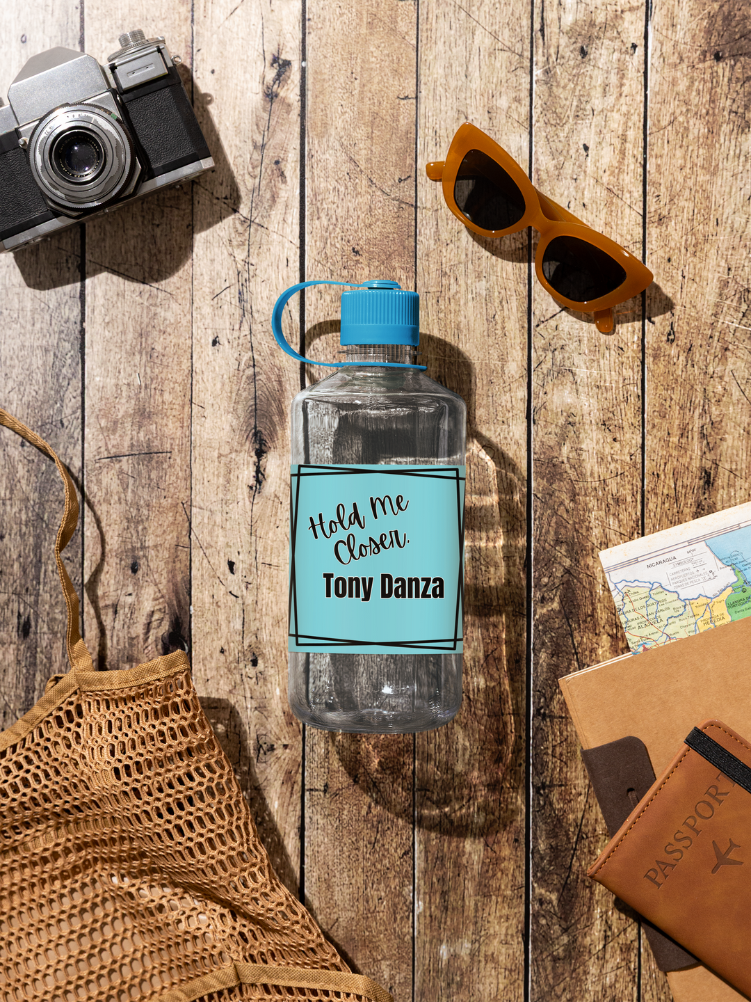 Clear water bottle with blue label on a wooden surface with camera, sunglasses, and passport holder.