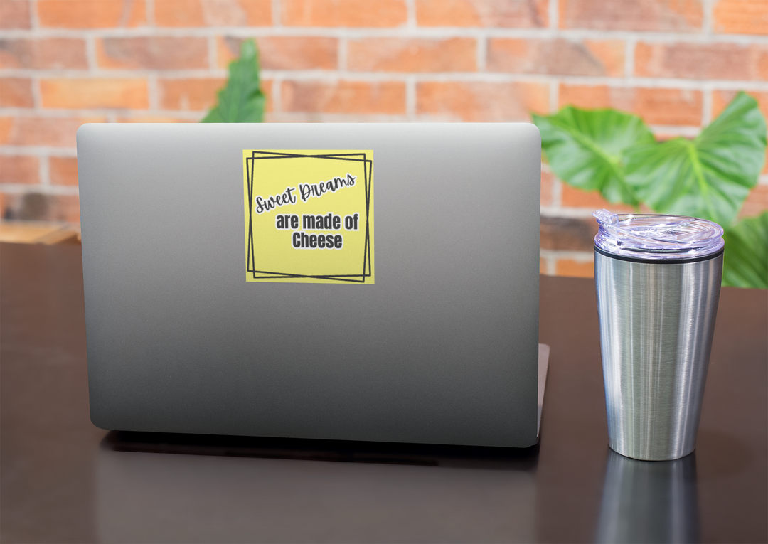 Laptop with a yellow sticker on a desk with a brick wall and plants in the background