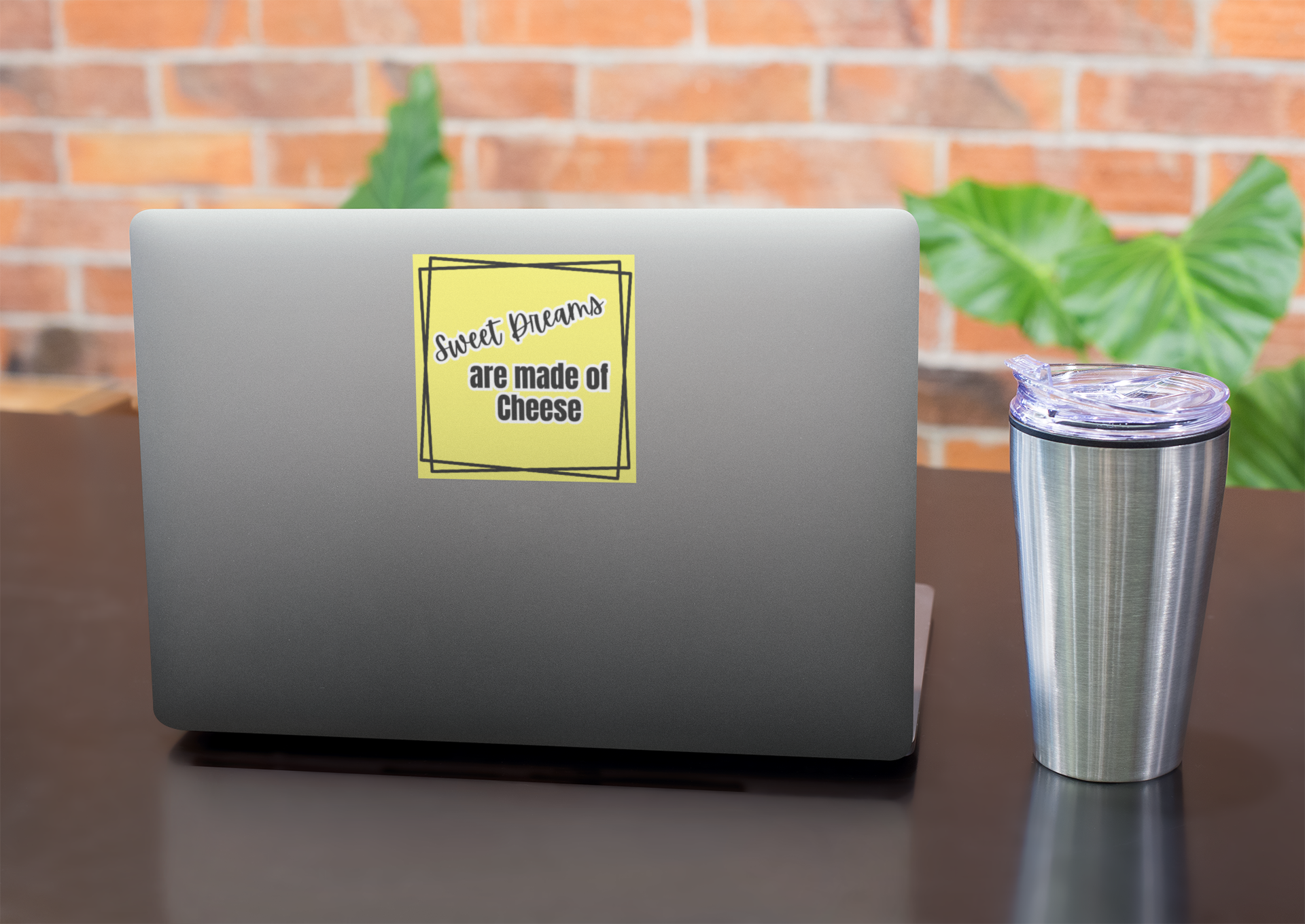 Laptop with a yellow sticker on a desk with a brick wall and plants in the background