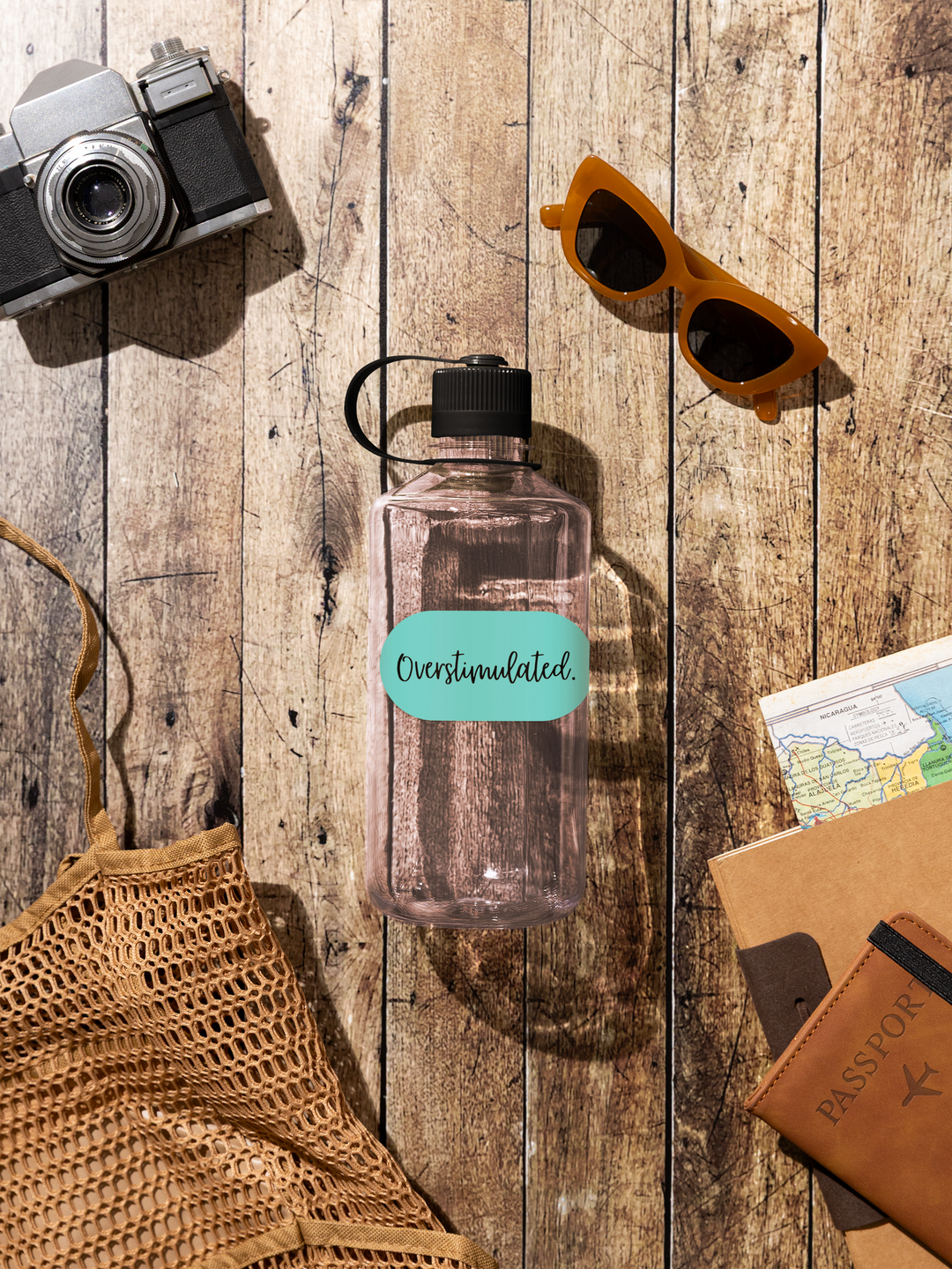 Clear water bottle with a teal label on a wooden surface with sunglasses, camera, and map.