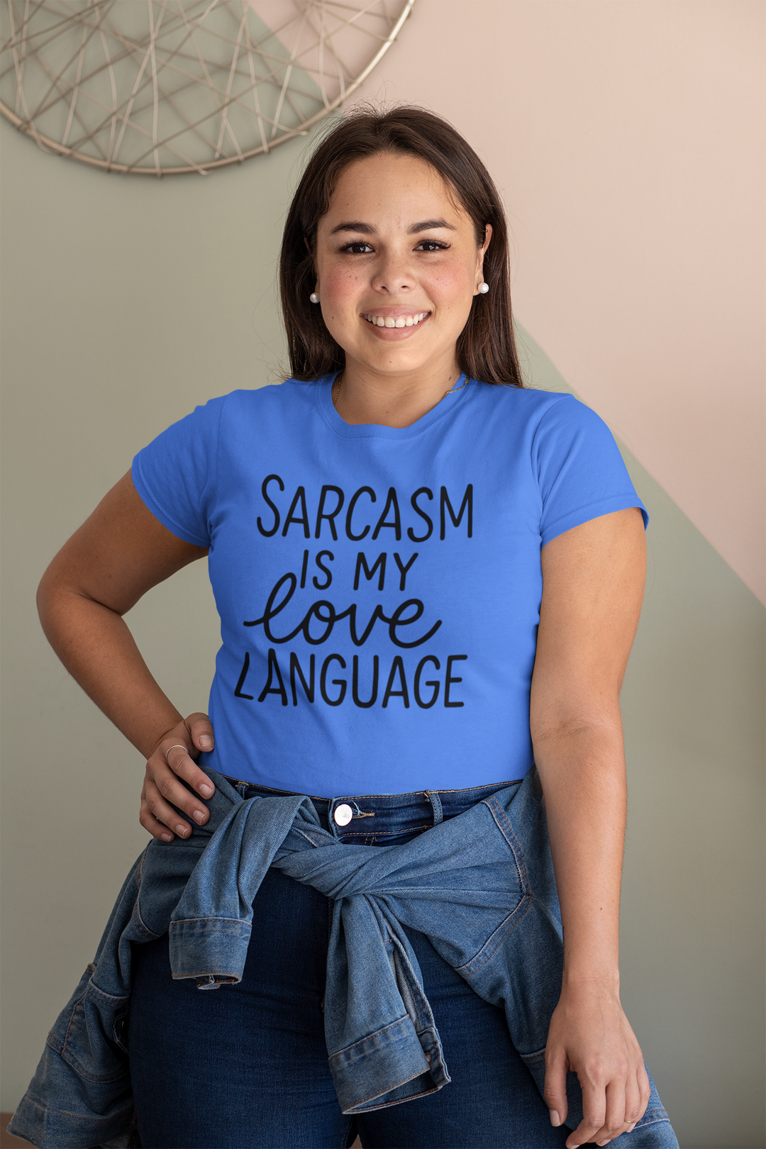Woman wearing a blue t-shirt with 'Sarcasm is my love language' text, standing against a neutral wall.
