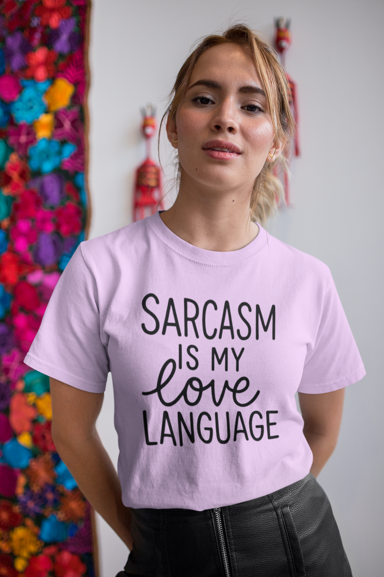 Person wearing a purple t-shirt with 'Sarcasm is my love language' text in front of colorful flowers.