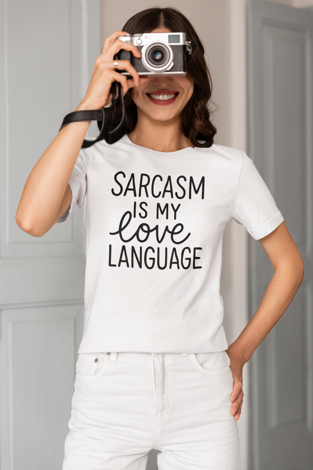 Person wearing a white t-shirt with 'Sarcasm is my love language' text, holding a camera.
