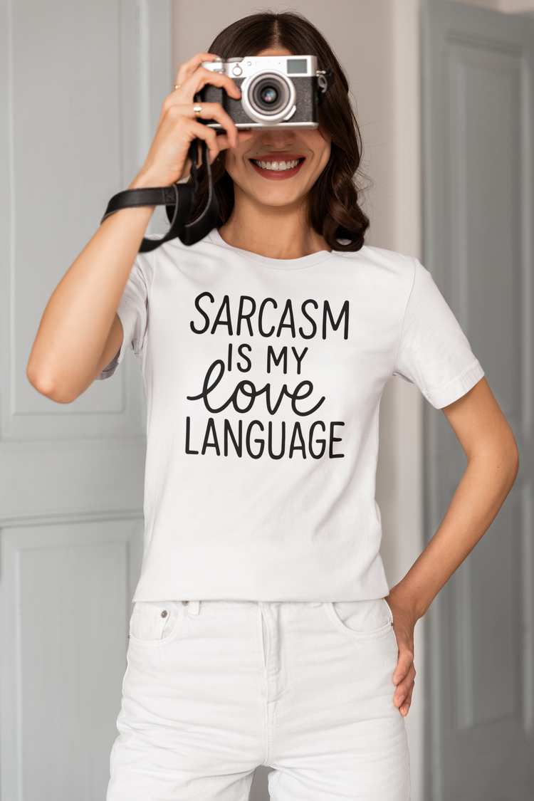 Person wearing a white t-shirt with 'Sarcasm is my love language' text, holding a camera.
