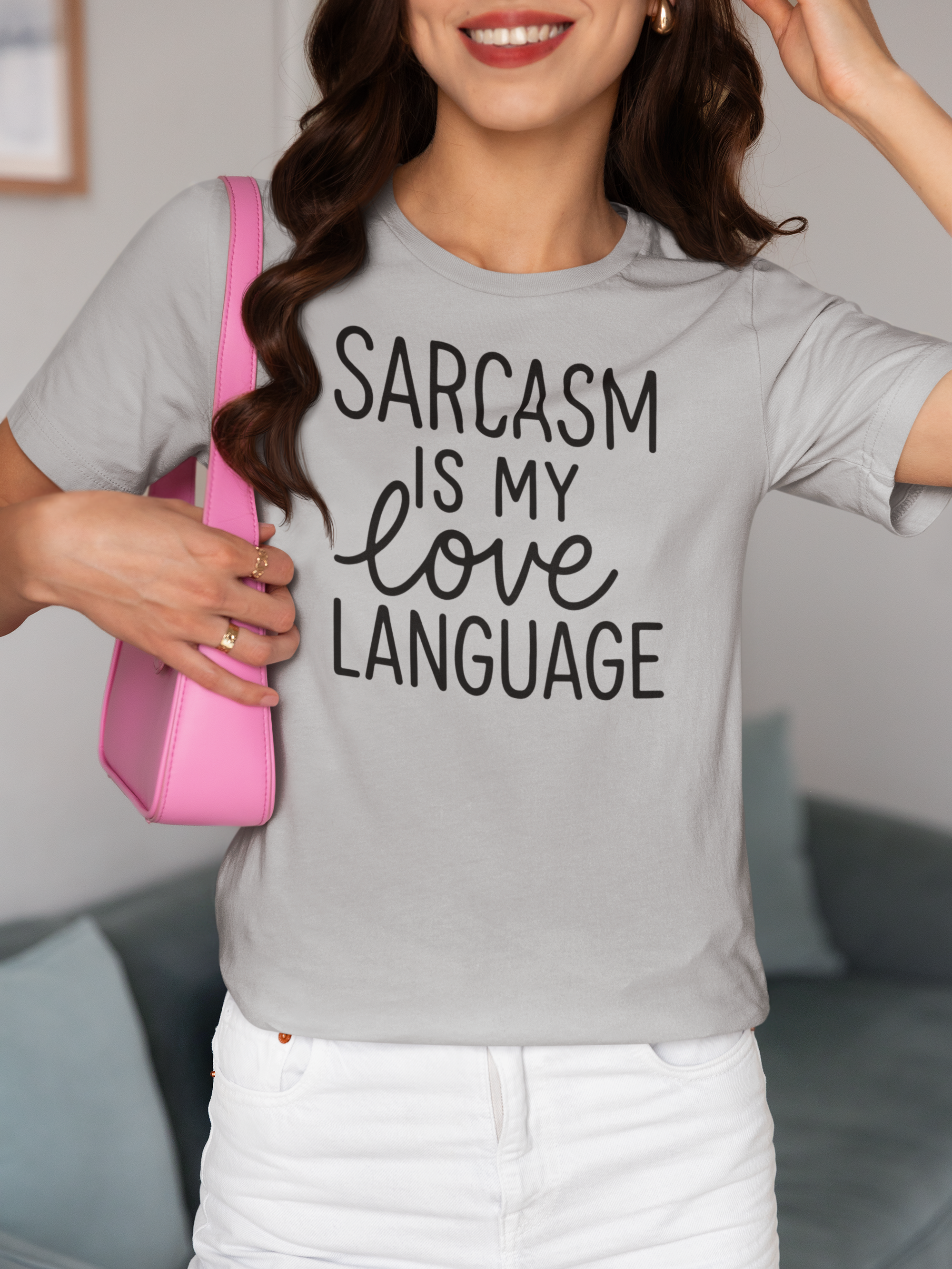 Person wearing a gray t-shirt with 'Sarcasm is my love language' text, holding a pink bag.