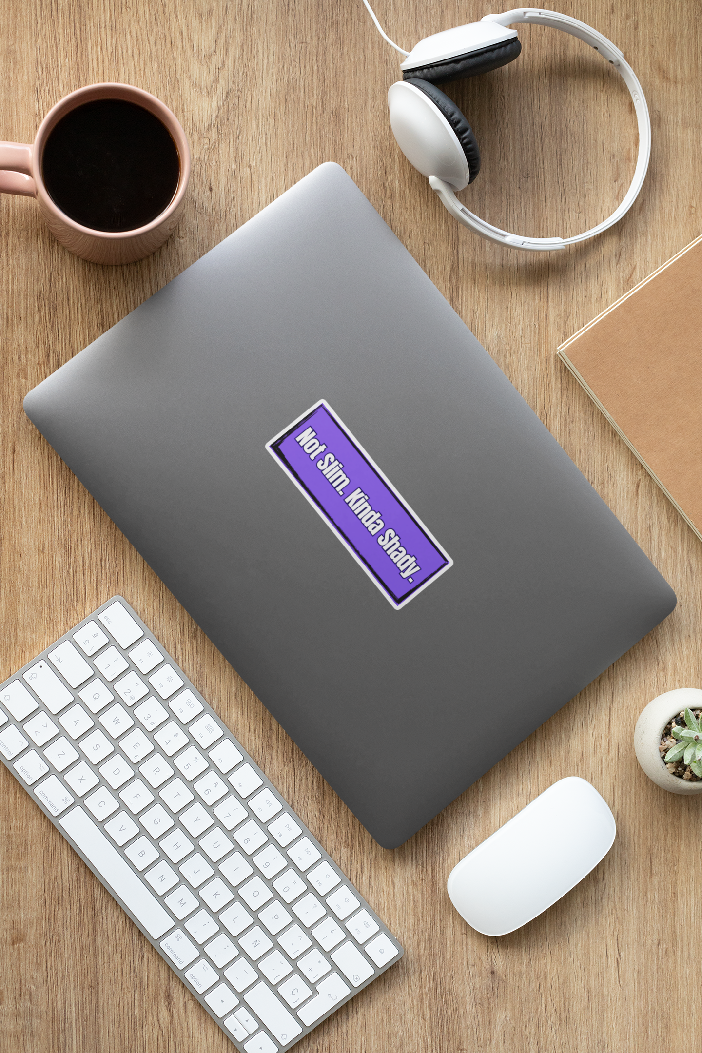 Gray laptop with a purple "Not Slim, Kinda Shady" sticker on a wooden desk with keyboard, mouse, and coffee cup.