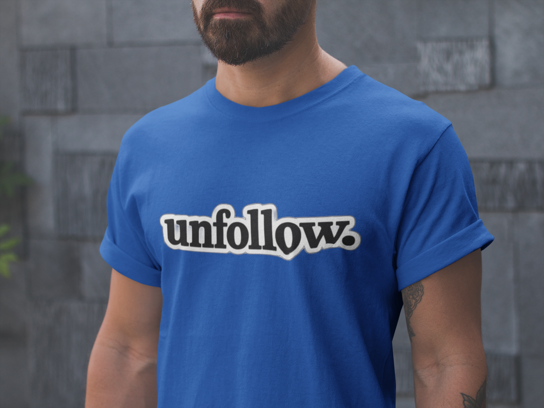 Person wearing a blue t-shirt with 'unfollow.' text against a gray stone wall.