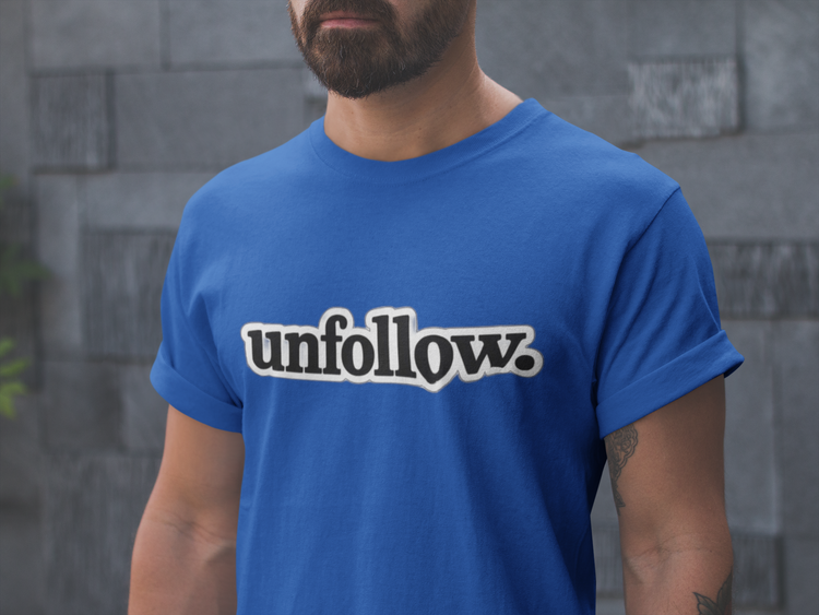 Person wearing a blue t-shirt with 'unfollow.' text against a gray stone wall.