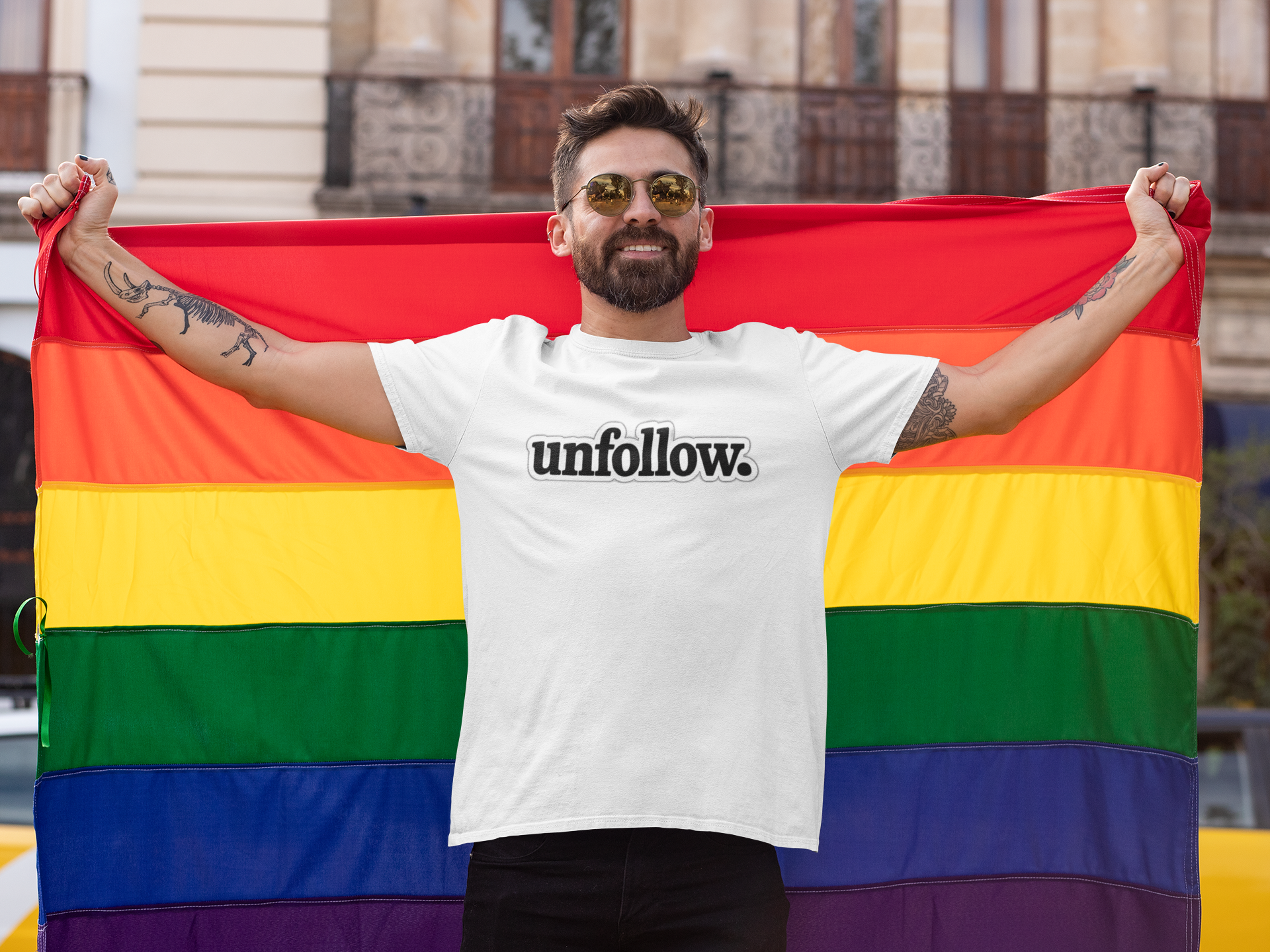 Person holding a rainbow flag wearing a white t-shirt with 'unfollow.' text.