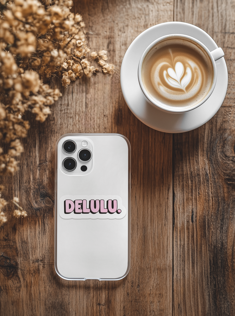 Phone case with 'DELULU' branding next to a cup of coffee on a wooden surface