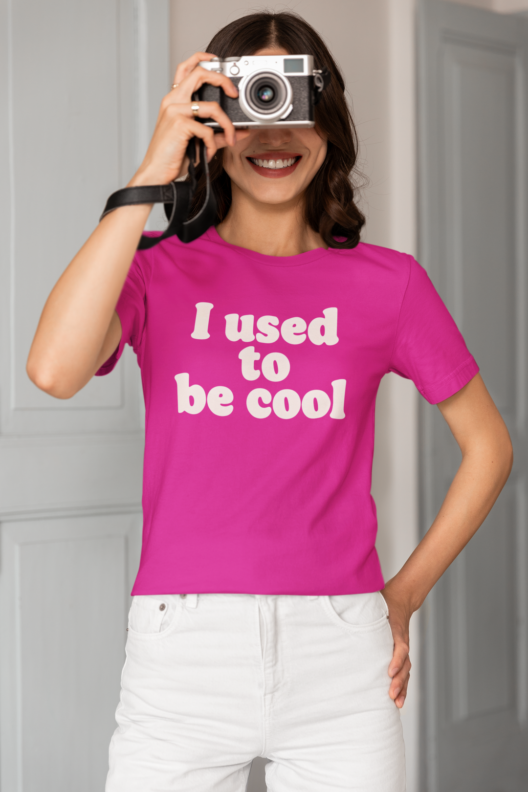Person wearing a pink t-shirt with 'I used to be cool' text, holding a camera.