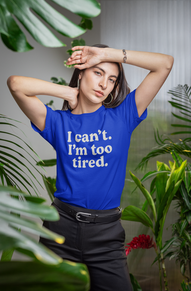 Woman wearing a blue t-shirt with 'I can't. I'm too tired.' text, surrounded by plants.