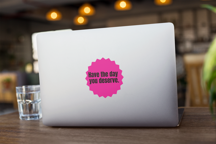Laptop with a pink "Have the day you deserve" sticker on a wooden table