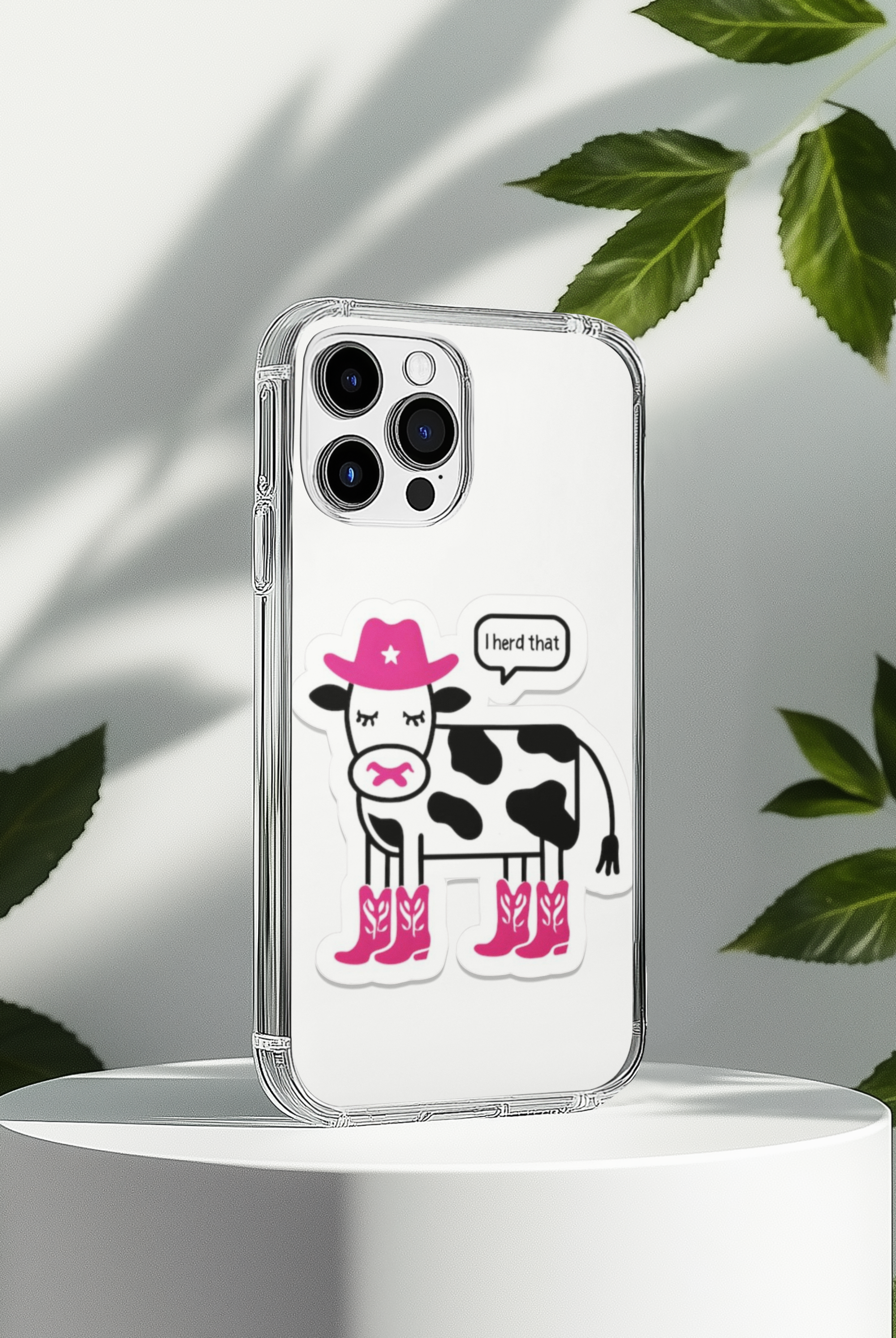 Phone case with a cow design wearing pink boots and a pink hat, on a white background with green leaves.