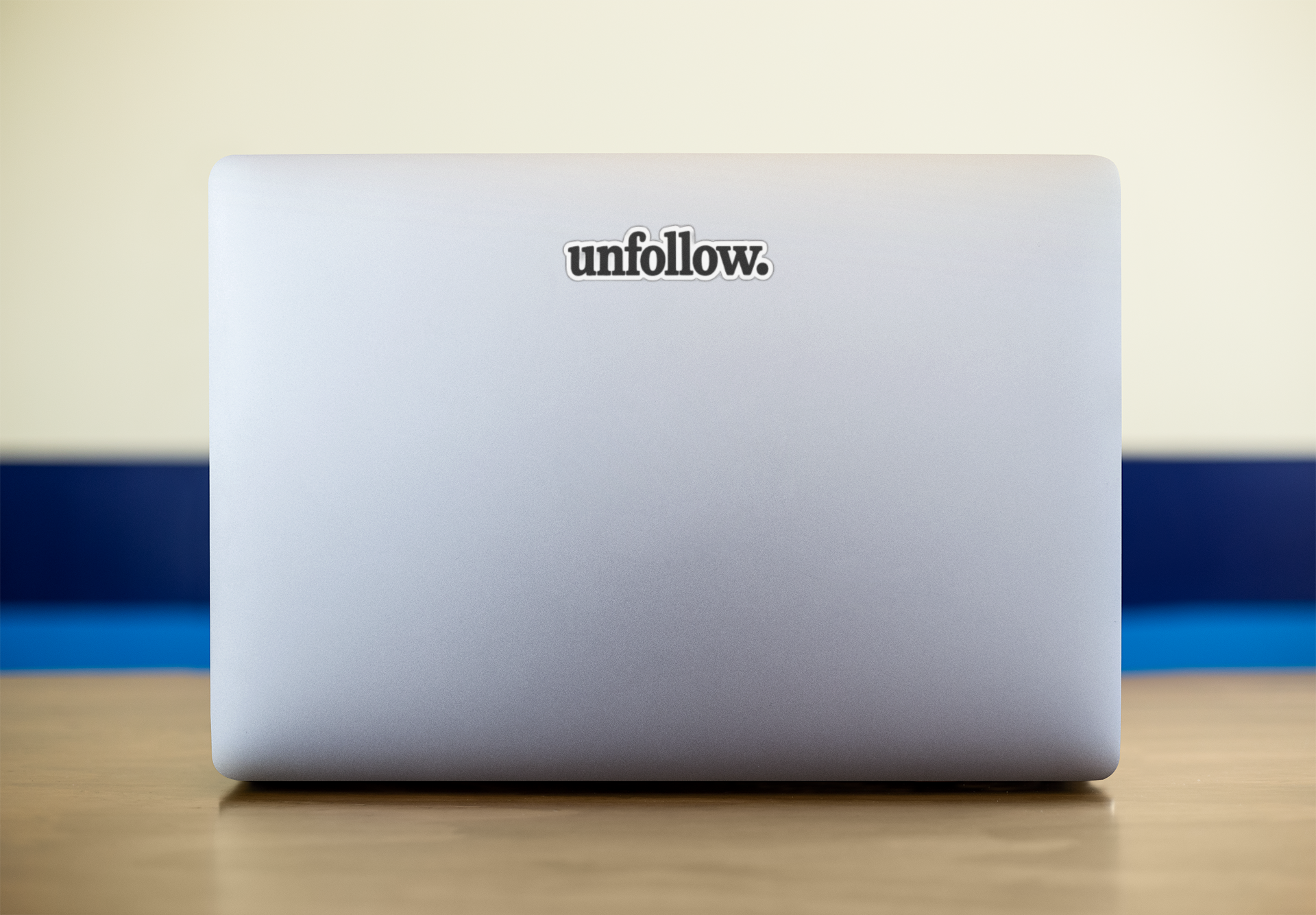 Laptop with 'unfollow.' sticker on a wooden surface with a blue and beige background