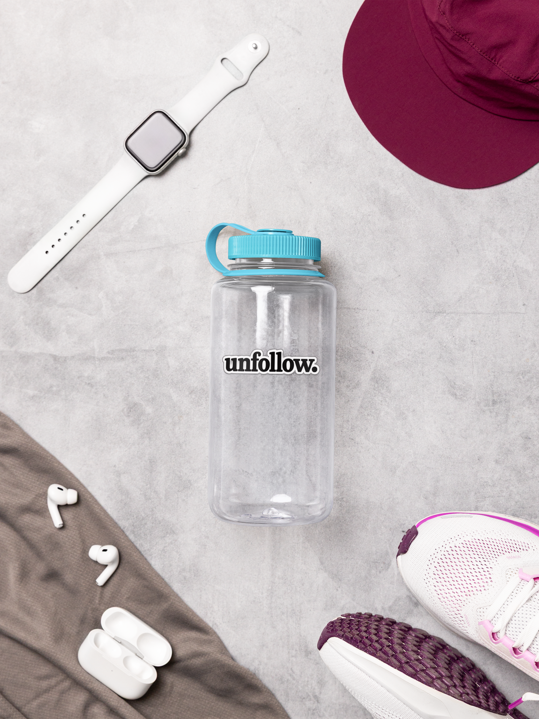 Clear water bottle with 'unfollow.' text, white smartwatch, maroon hat, white earbuds, and white sneakers on a light gray surface.