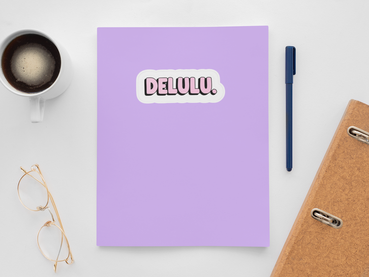 Purple notebook with a sticker reading 'DELULU', next to a cup of coffee, glasses, and a pen on a white surface.
