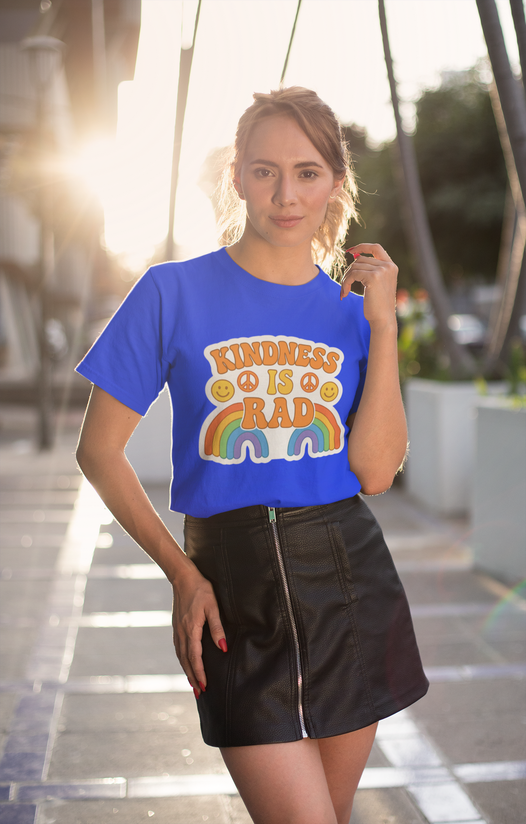 Woman wearing a blue t-shirt with a Kindness Is Rad shirt, standing outdoors.