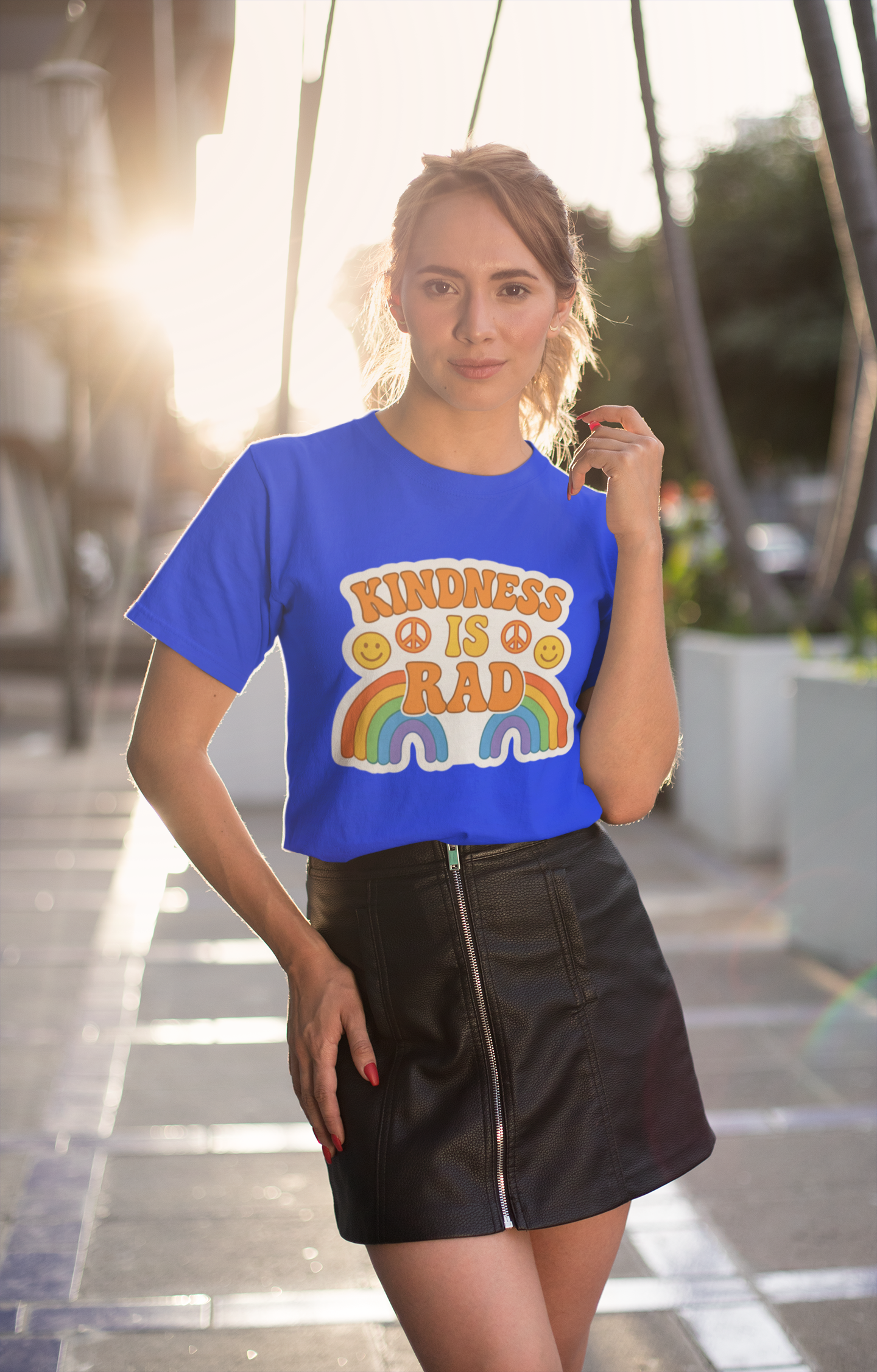 Woman wearing a blue t-shirt with a Kindness Is Rad shirt, standing outdoors.