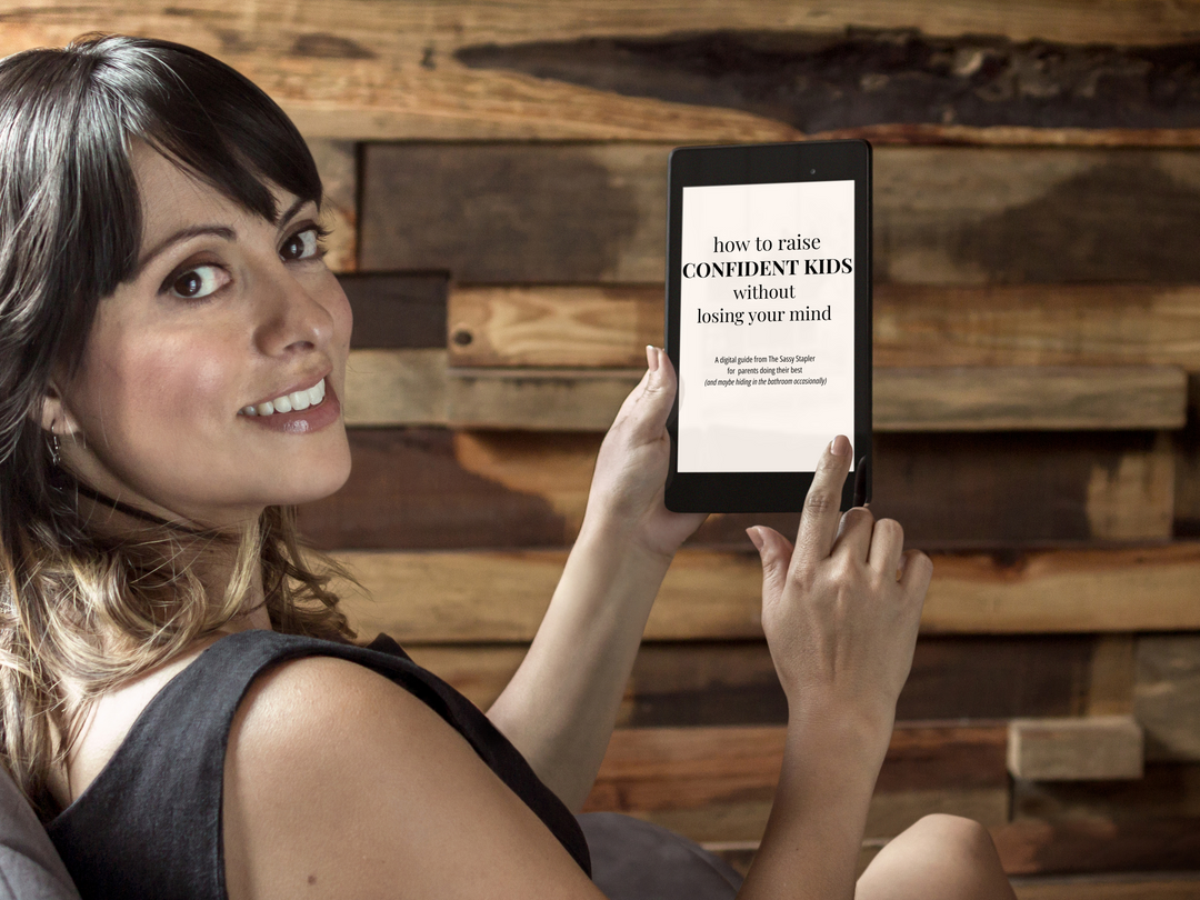 Woman holding a tablet with text 'how to raise CONFIDENT KIDS without losing your mind' against a wooden background