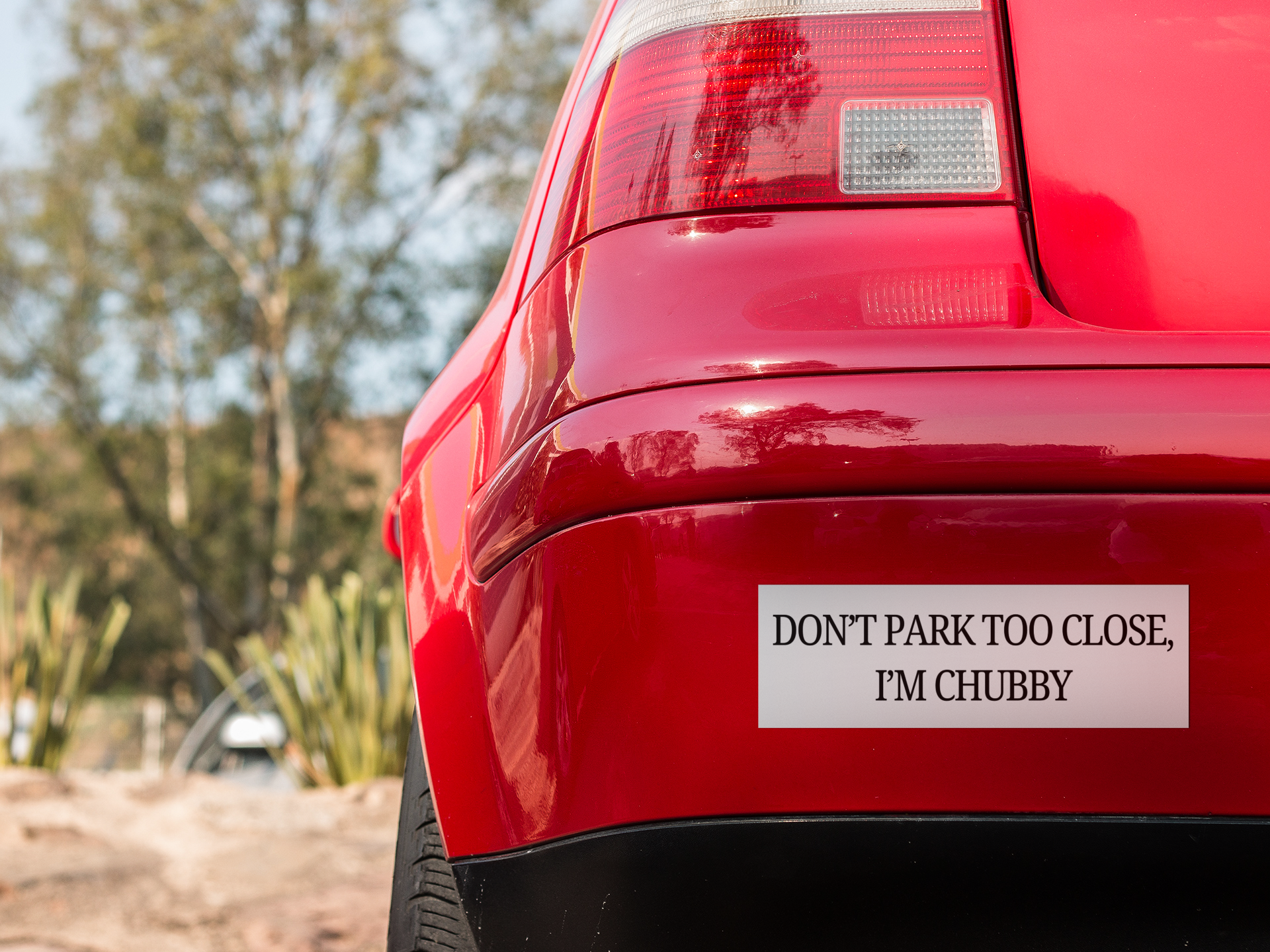 Red car with a humorous bumper sticker, "Dont park Too Close, I'm Chubby" on a natural background