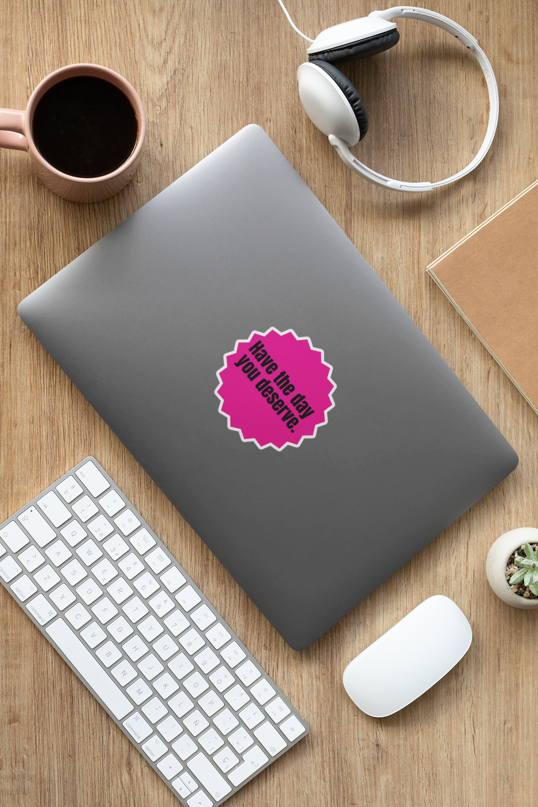 Laptop with a pink "Have the day you deserve" sticker on a wooden desk with keyboard, mouse, and coffee cup.