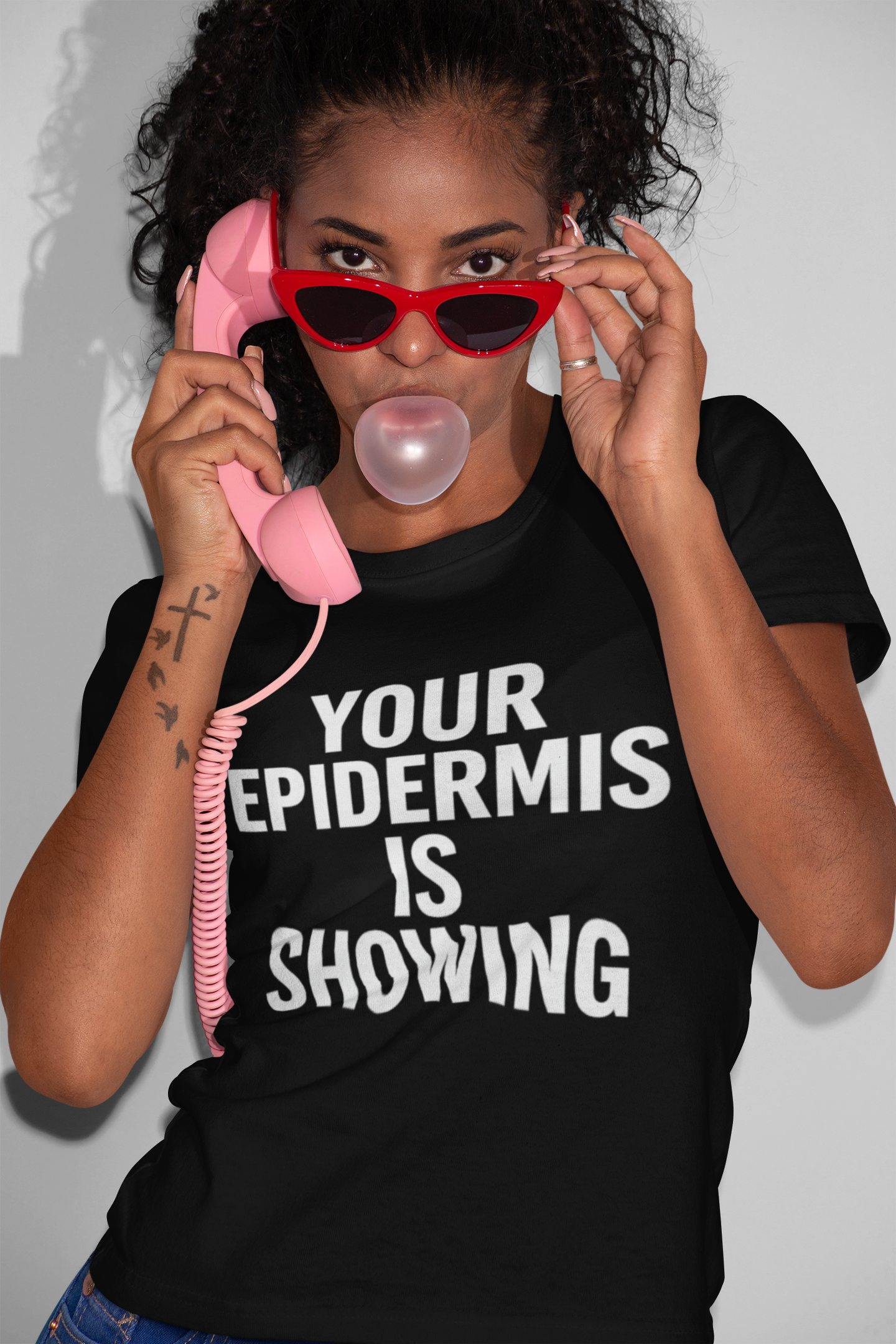Person wearing a black t-shirt with 'Your Epidermis is Showing' text, holding a pink phone to their ear.
