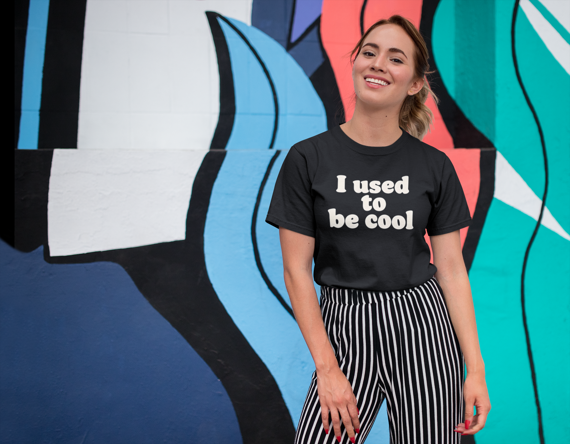 Person wearing a black t-shirt with 'I used to be cool' text in front of a colorful abstract mural.